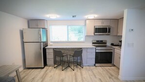 A compact kitchen with a refrigerator, microwave, oven, and two bar stools. - Seashell Room Manasota Delux Villas (Sarasota County)