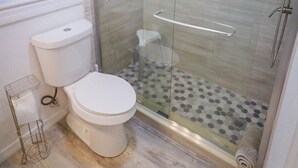 A modern bathroom with a glass-enclosed shower, a toilet, and a window. - Seashell Room Manasota Delux Villas (Sarasota County)