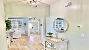 A hallway with a white console table, a round mirror, and a ceiling fan. - Saltee Cove Coastal Getaway - Charming 3 Bedroom/2.5 Bath Lowcountry Cottage (Bluffton)