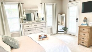 A bedroom with a bed, a dresser, a mirror, and a television on the wall. - Saltee Cove Coastal Getaway - Charming 3 Bedroom/2.5 Bath Lowcountry Cottage (Bluffton)