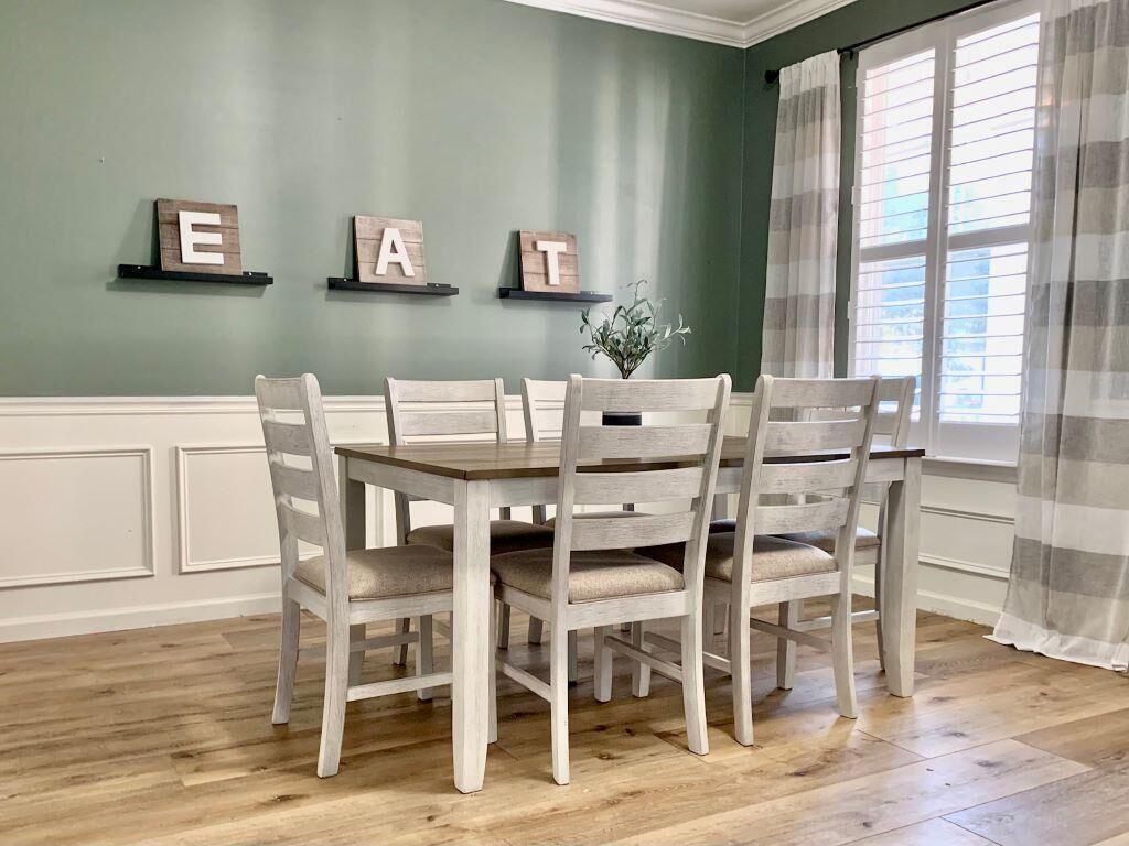 Un comedor con una mesa de madera y seis sillas, una pared verde y una ventana con cortinas.