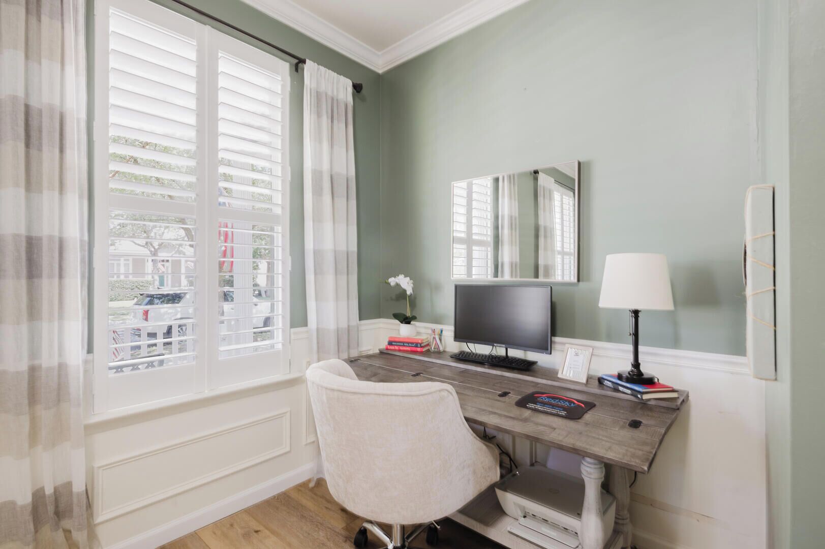 A room with a desk, chair, computer, lamp, and a window with blinds.