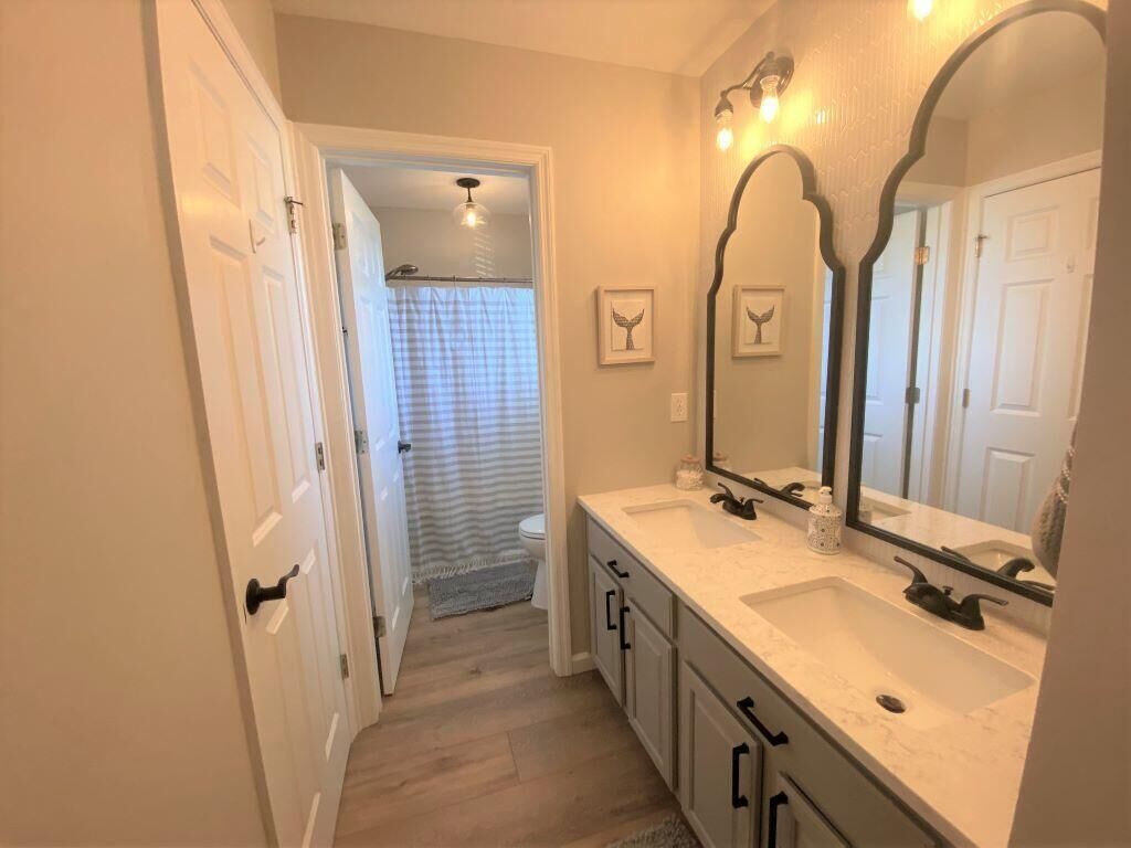 Un baño con lavamanos doble, un espejo grande y una zona de ducha visible a través de una puerta abierta.