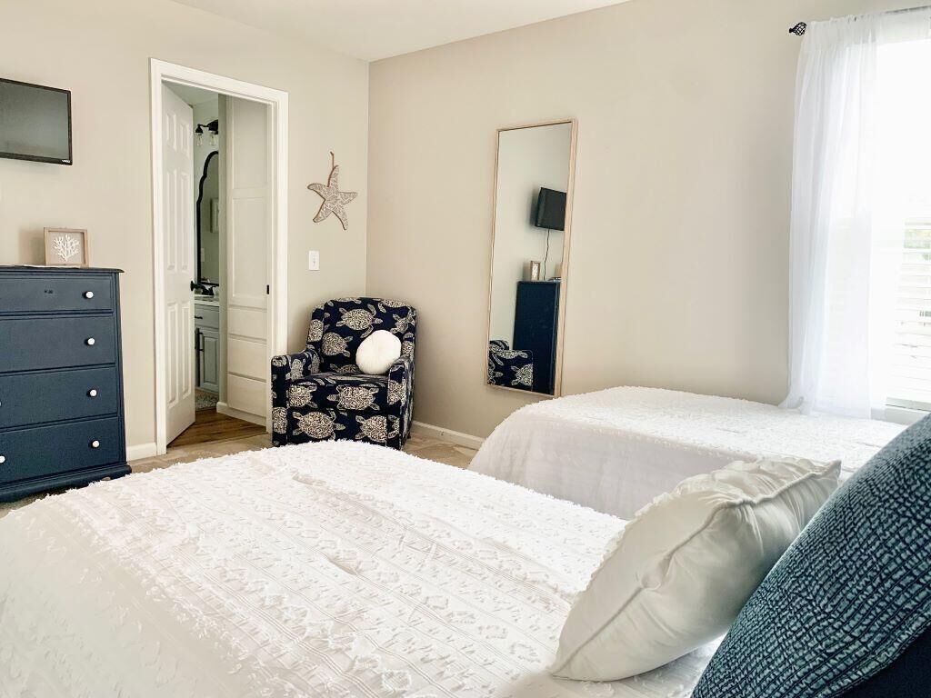 A bedroom with two beds, a dresser, a chair, a mirror, and a star decoration on the wall.