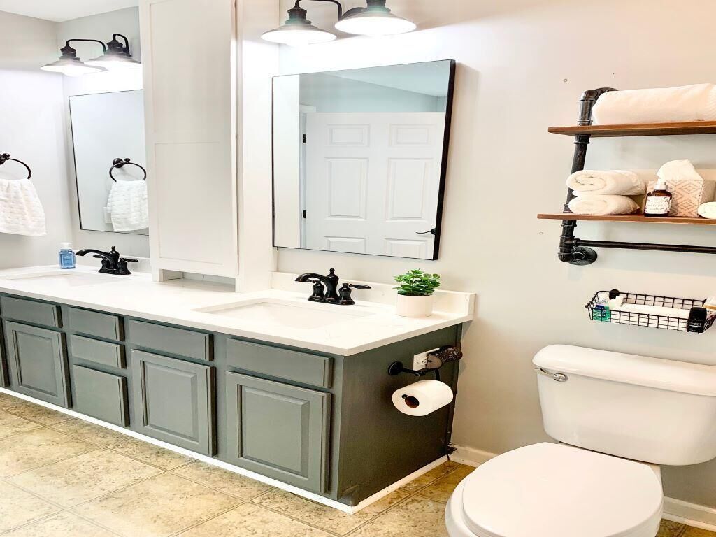 A bathroom with a double sink vanity, a toilet, a large mirror, and shelves with towels and toiletries.