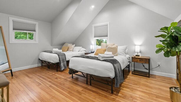 Une chambre avec deux lits, un plancher en bois, des murs blancs et un plafond en pente.