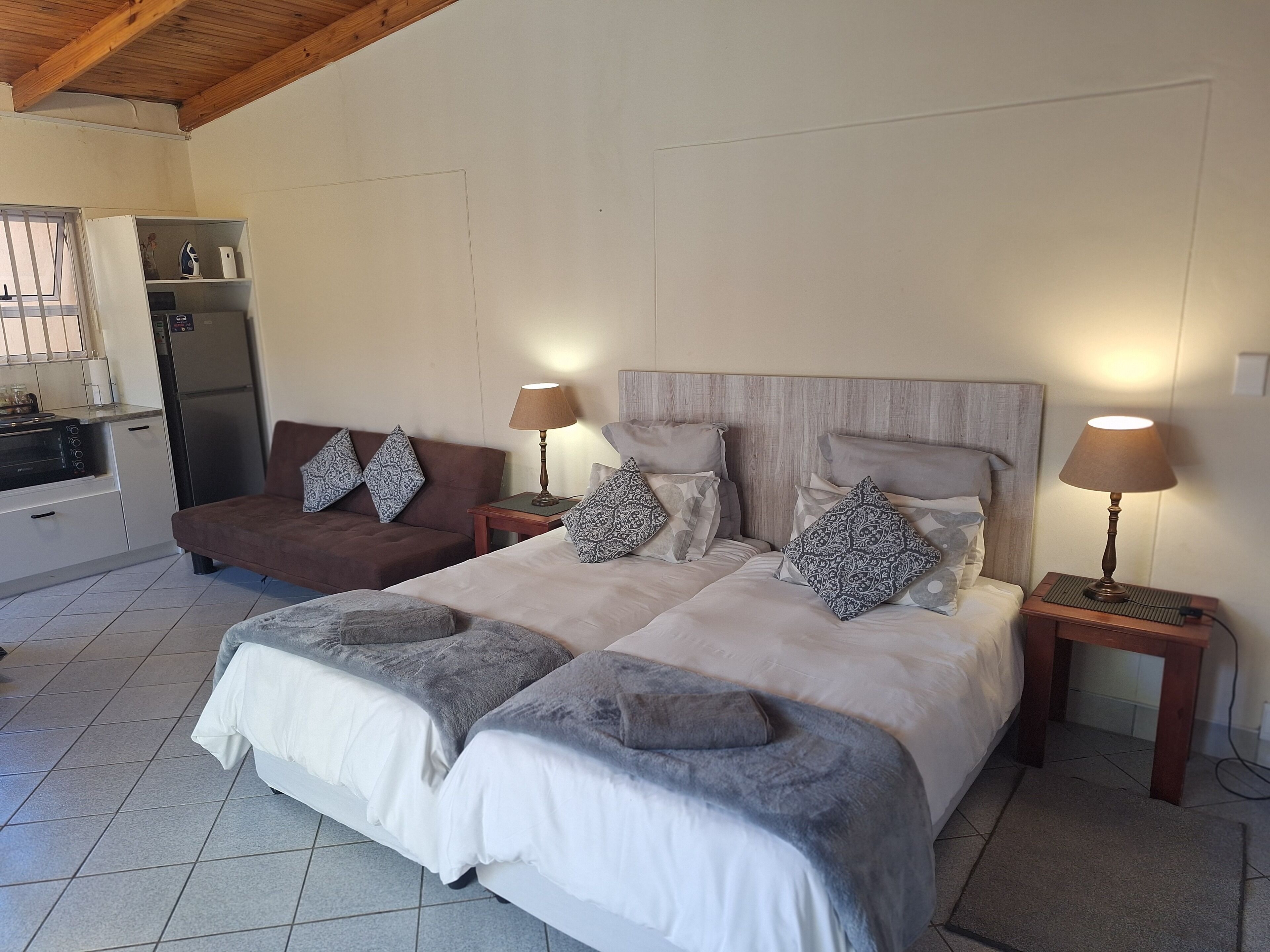 Een slaapkamer met twee bedden, een bank, een keukenhoek en een houten plafond.