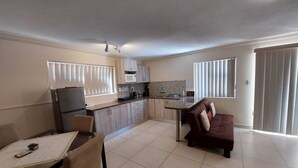 A compact kitchen with a refrigerator, microwave, and a coffee maker. There is a dining area with a table and chairs, and a sofa in the living room. - Spacious cosy, self- Catering loft with own entrance in safe & secure area. (Swakopmund)