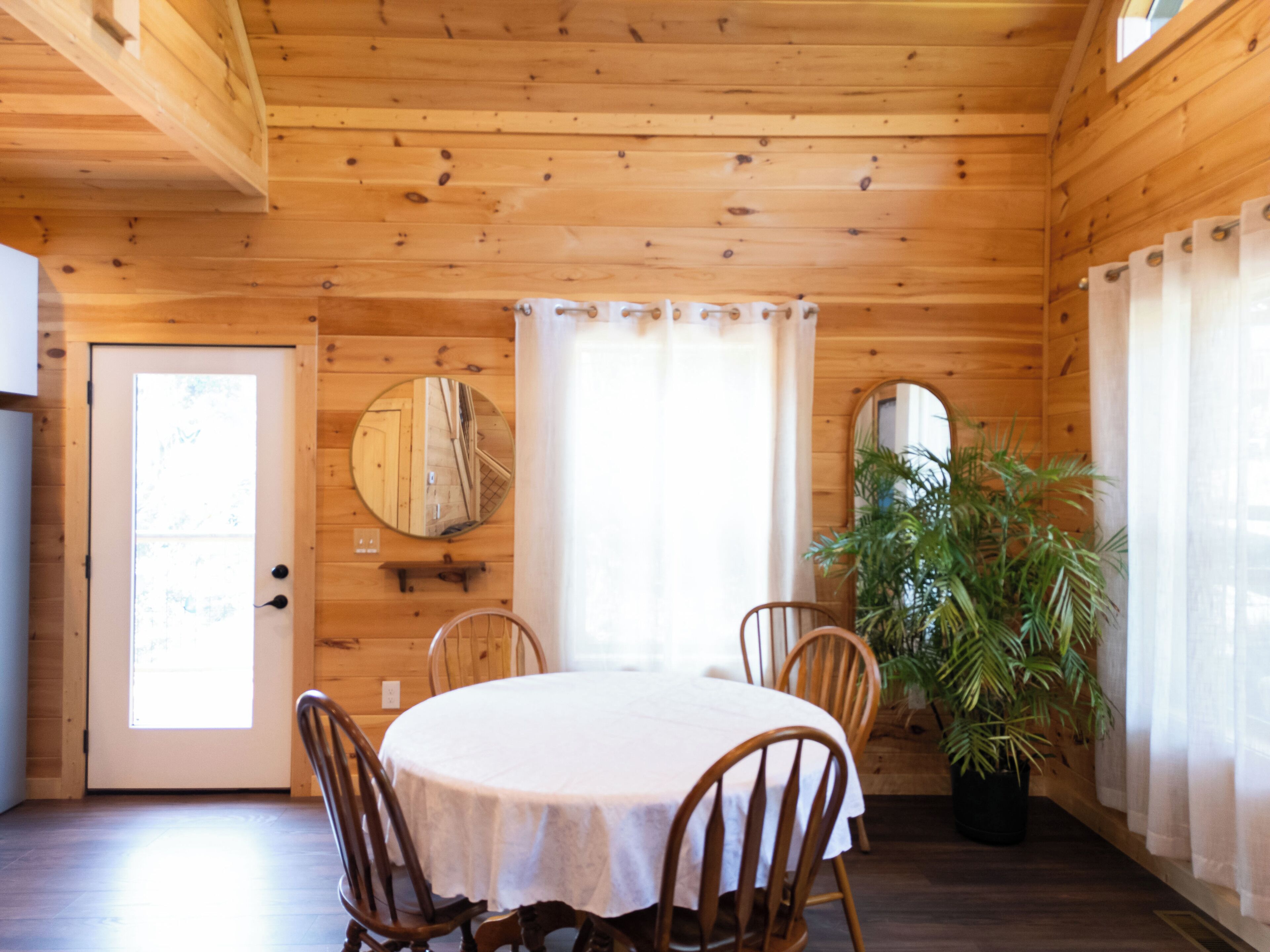 Un intérieur en bois avec une table ronde, des chaises, une porte et une plante en pot.