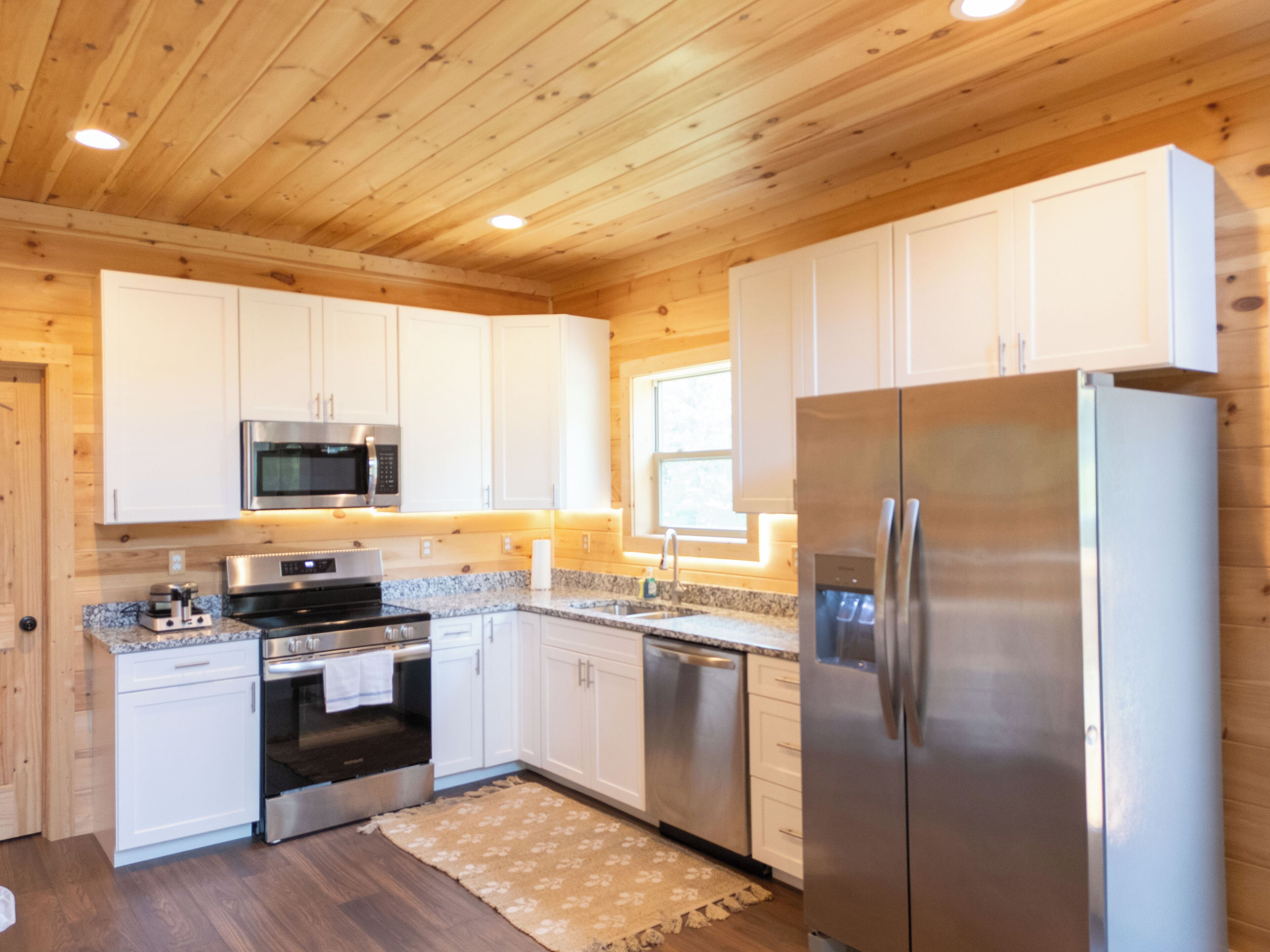 A modern kitchen with wooden ceiling, white cabinets, stainless steel appliances, and a granite countertop.