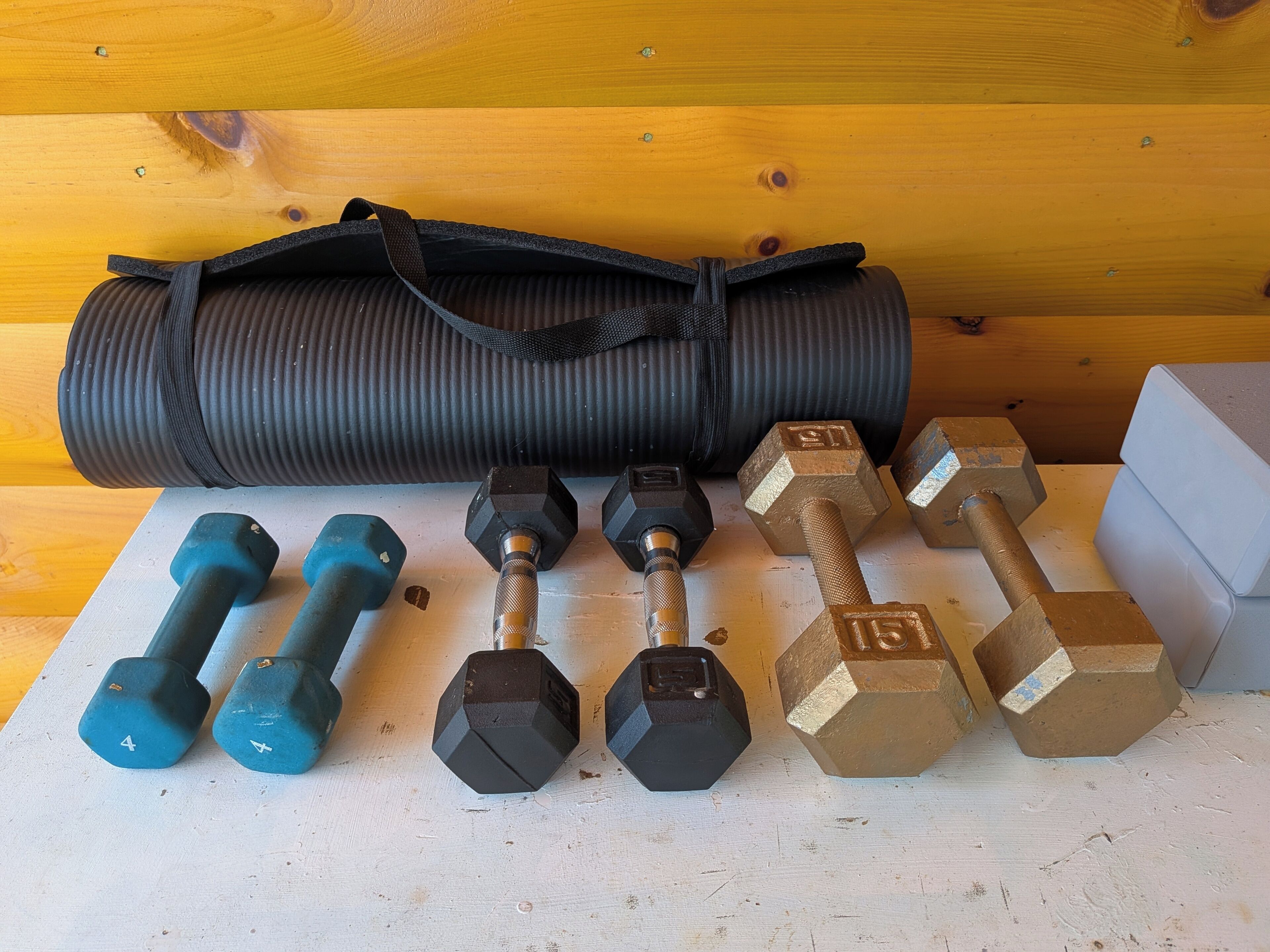 A set of dumbbells, a yoga mat, and a weight bench on a wooden floor.