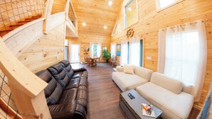 Un interior de madera con un sofá de cuero negro, un sofá blanco, una mesa de comedor y una escalera.