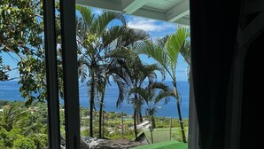 Blick aus einem Zimmer mit großem Fenster auf einen Swimmingpool, umgeben von Palmen und mit Meerblick.