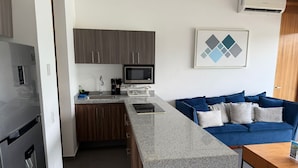 A modern kitchen with a built-in microwave, a sink, and a countertop. There is a blue sofa with cushions in the living area. - Seaside getaway in B Nayar (Cruz de Huanacaxtle)
