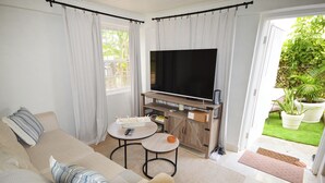Un salón con sofá, mesa de centro y mueble para televisión. Hay una puerta corredera de vidrio que da a un jardín.