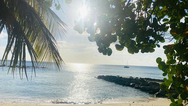 Una playa con agua cristalina, un velero y un promontorio rocoso.
