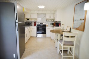A compact kitchen with white cabinets, a stainless steel refrigerator, a built-in oven, and a dining area with a wooden table and white chairs.