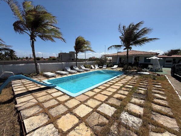 A swimming pool with lounge chairs, palm trees, and a building with a tiled roof.