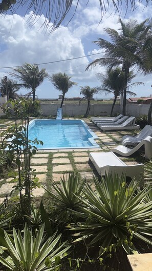 A swimming pool with lounge chairs, surrounded by palm trees and plants.