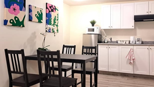 A dining area with a wooden table and chairs, a kitchen with white cabinets, and colorful abstract wall art. - Entire basement, close to CTrain (Calgary)