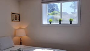 A bedroom with a bed, a bedside lamp, a window with plants, and a framed picture on the wall. - Entire basement, close to CTrain (Calgary)