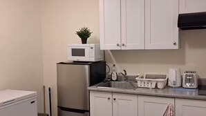 A compact kitchen with white cabinets, a stainless steel refrigerator, a microwave, a sink with a dish rack, and a toaster. - Entire basement, close to CTrain (Calgary)