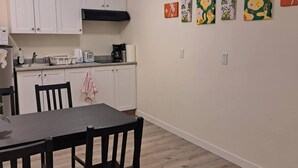 A compact kitchen with white cabinets, a black range hood, and a dining area with a dark table and chairs. - Entire basement, close to CTrain (Calgary)