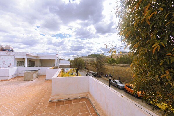 A rooftop terrace with a view of the street, a concrete bench, and a tiled floor.