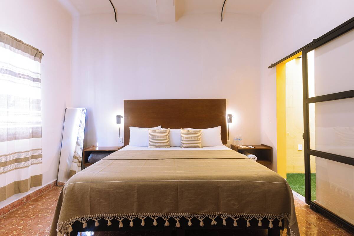 Habitación de hotel con una cama grande, una mesita de noche, una lámpara y un balcón con puerta corredera.