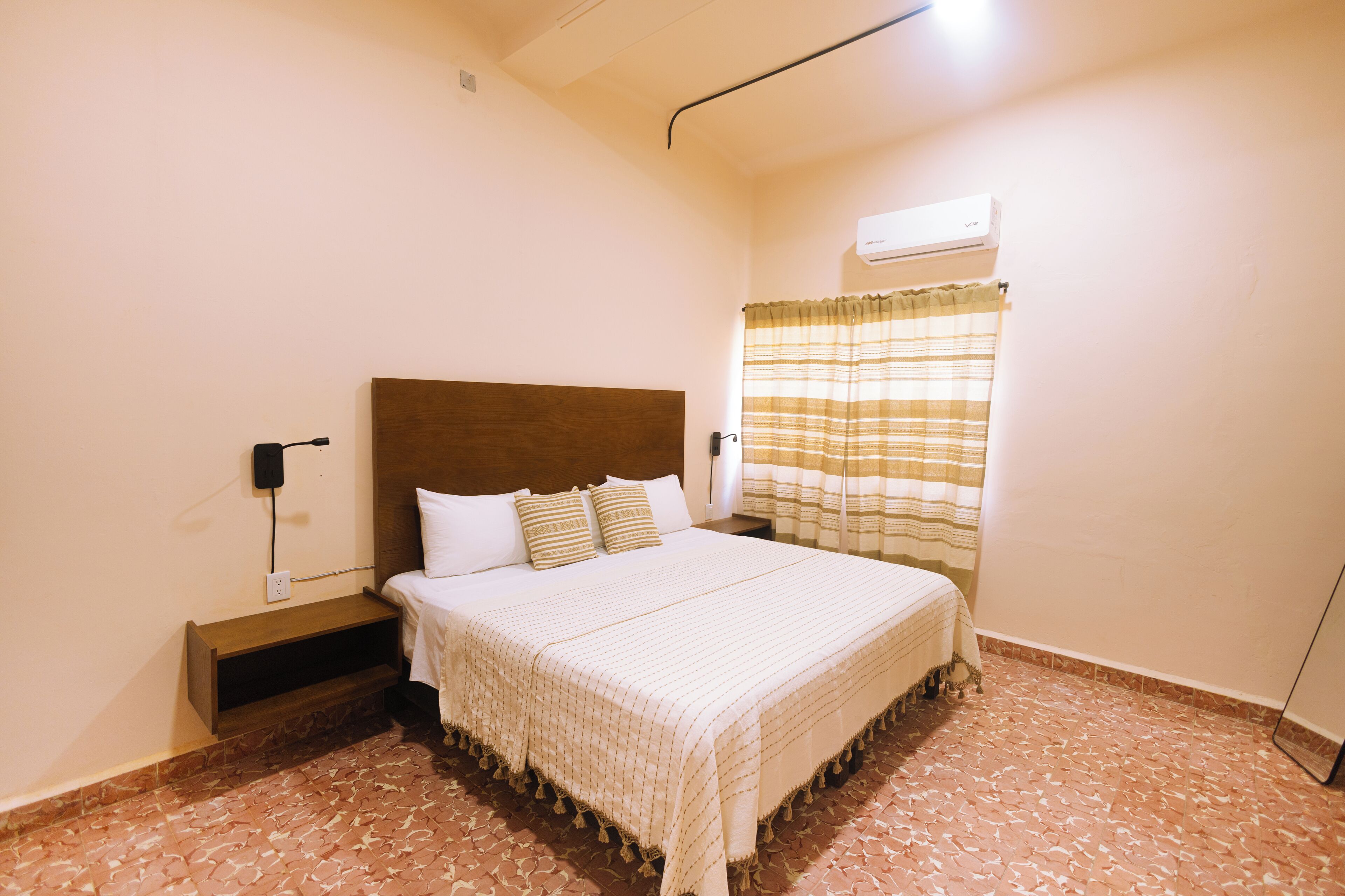 A neatly made bed with a wooden headboard, a bedside table, and a wall-mounted air conditioner.