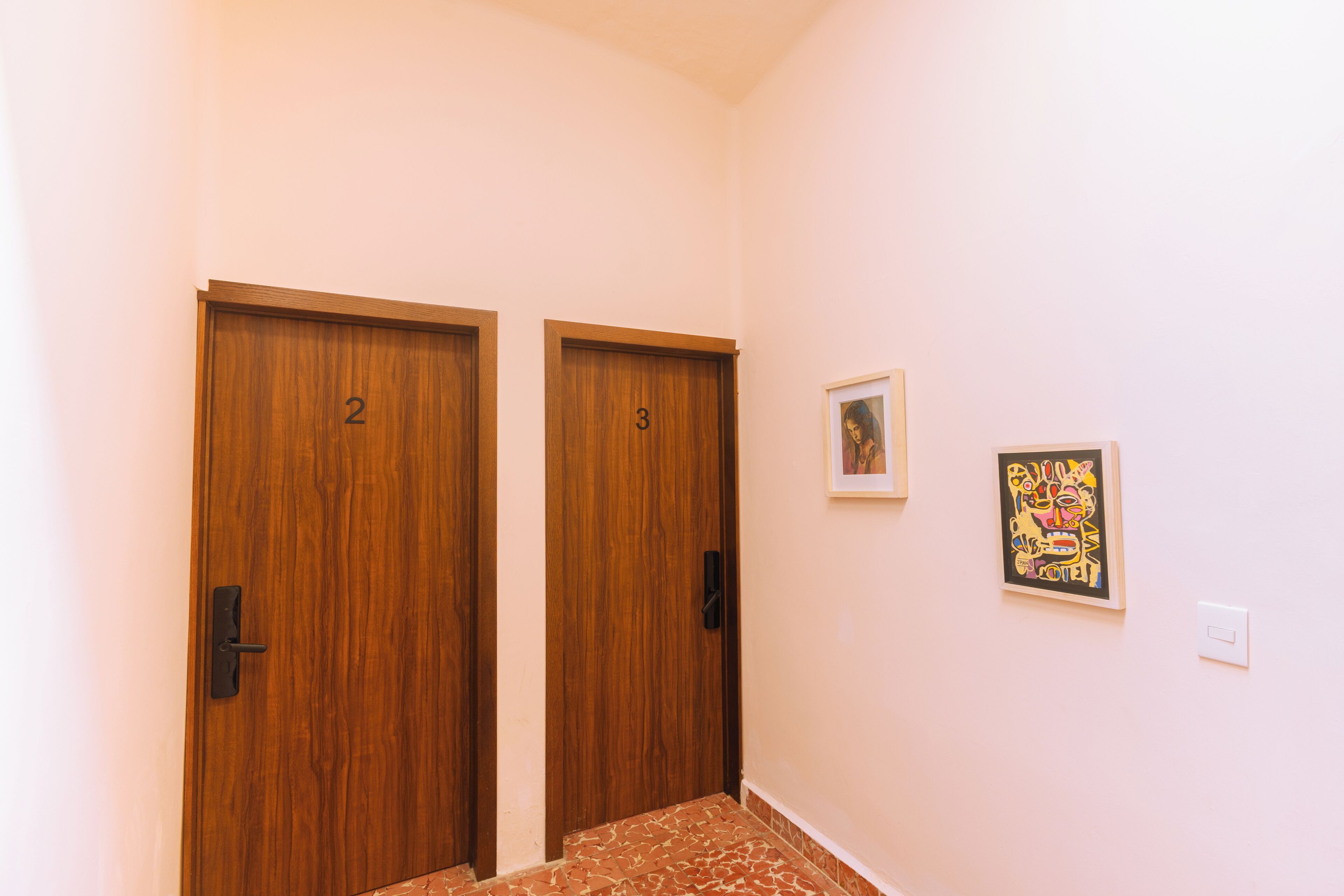 Un pasillo con dos puertas de madera, numeradas 2 y 3, y una obra enmarcada en la pared.