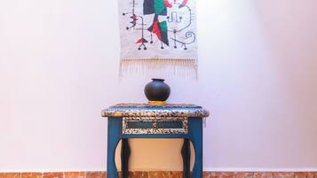 Una mesa azul con una superficie decorativa y un florero negro encima, frente a una pared con un tapiz colorido.