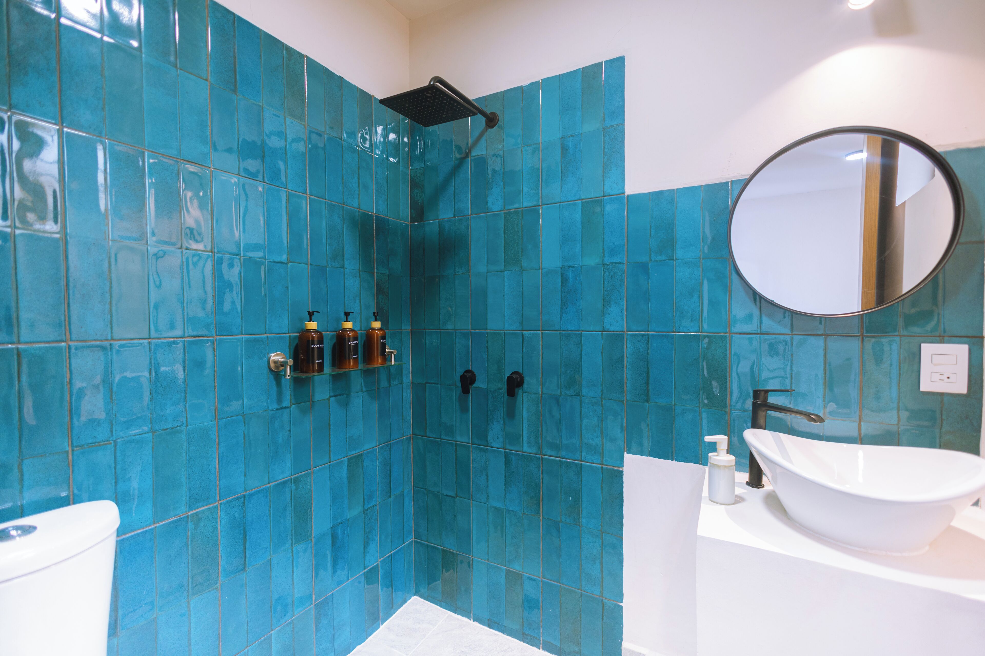 A bathroom with blue tiles, a white sink, a round mirror, and a shower area.