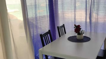 Un comedor con una mesa blanca, sillas negras y un florero con flores rojas.