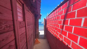 A narrow corridor with wooden walls and a red brick wall, leading to a beach view.