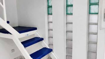A staircase with blue steps leading to a landing, white walls, and a marble floor.