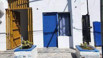 A building with a white facade and blue doors, featuring a wooden gate and a small garden area.