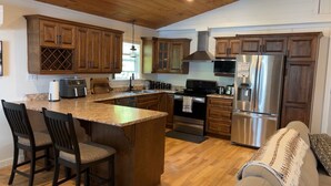 A kitchen with wooden cabinets, stainless steel appliances, a granite countertop, and a central island with bar stools. - Welcome to Sunset Cove, Cozy home, enjoy the landscaped property & outdoor area. (Goobies)