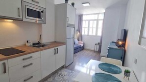 Eine moderne Küche mit weißen Schränken, einer Mikrowelle und einem Kühlschrank. Es gibt einen Essbereich mit einem weißen Tisch und blauen Tischsets.