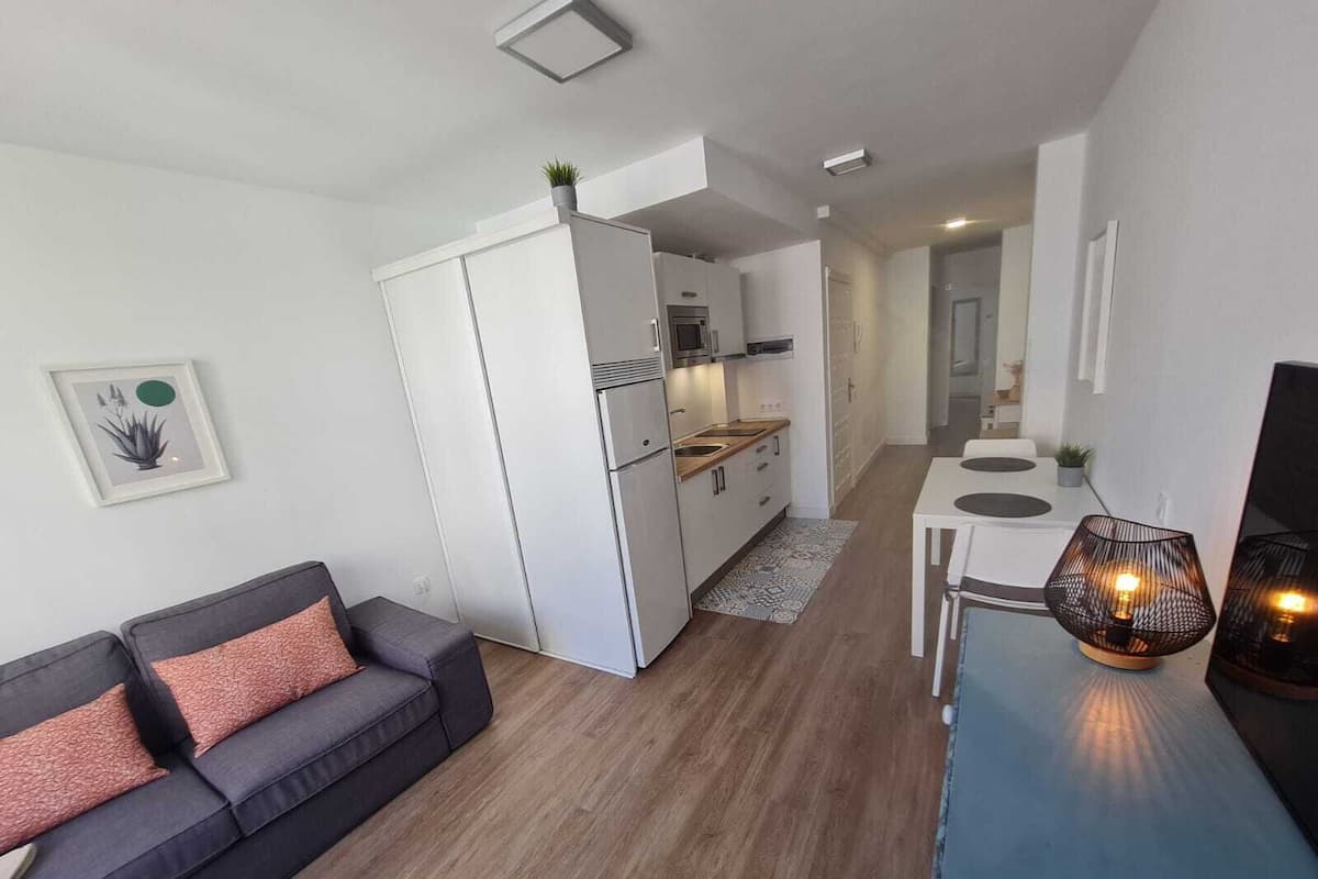 A modern apartment with a grey sofa, a dining table, and a kitchen area.