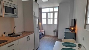 Eine kompakte Küche mit Mikrowelle, Spüle und Kühlschrank. Es gibt eine Essecke mit Tisch und Stühlen sowie eine kleine Sitzecke mit einer Couch.