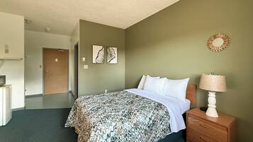Une chambre d’hôtel comprenant un lit, une table de chevet avec une lampe, une commode et une porte donnant sur une autre pièce.