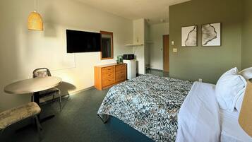 A hotel room with a bed, a desk, a chair, a dresser, a television, and artwork on the walls.
