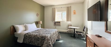 Una habitación de hotel con una cama, un escritorio, una silla, un televisor y un aparador.