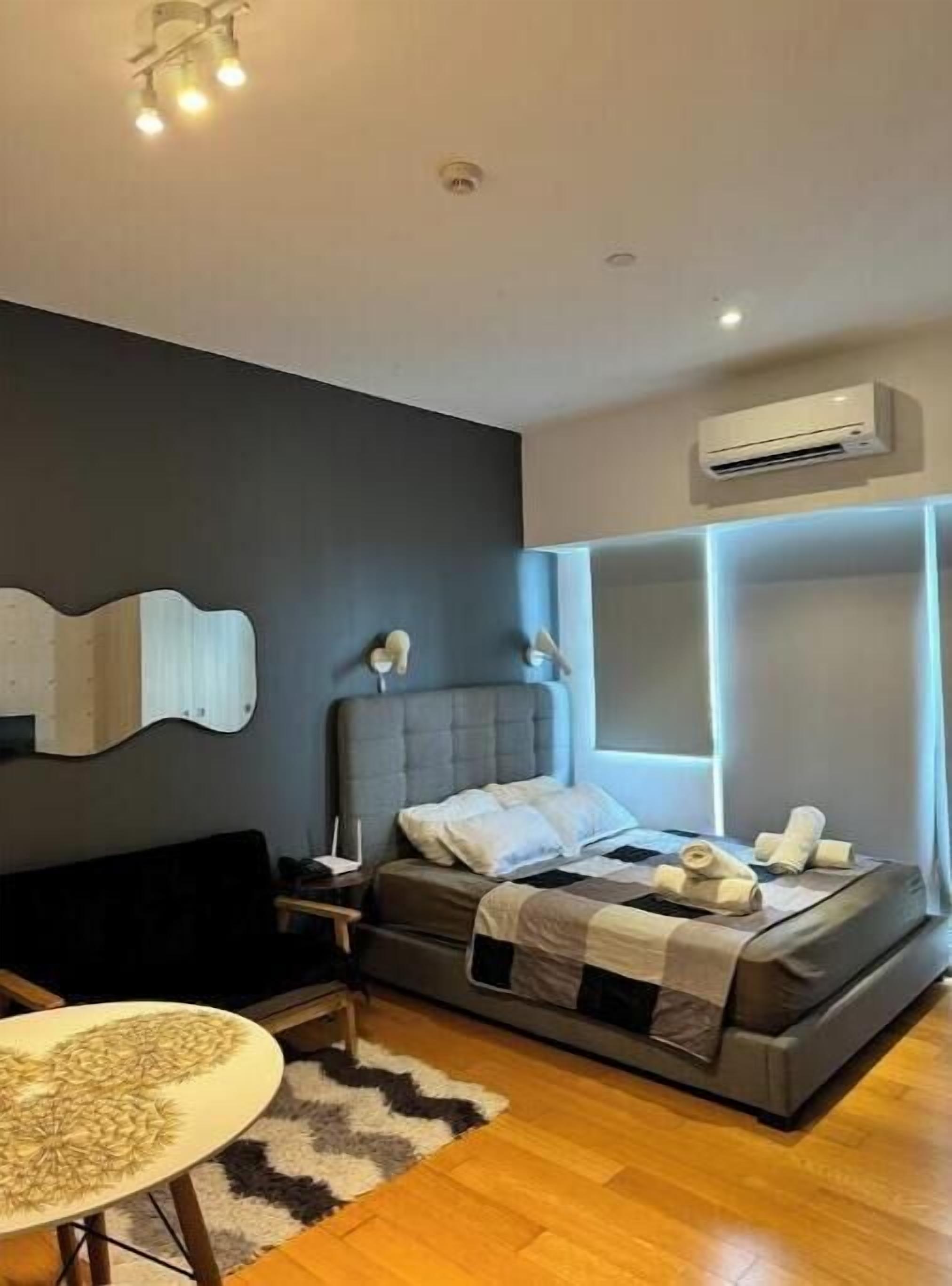A modern bedroom with a bed, bedside tables, a small round table, and an air conditioning unit.
