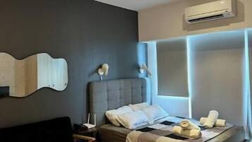 A modern bedroom with a bed, bedside tables, a small round table, and an air conditioning unit.