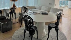 Un salon moderne avec une table ronde blanche, des chaises noires et un canapé blanc. De grandes fenêtres laissent entrer la lumière naturelle et offrent une vue sur la ville.