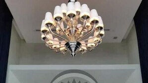 Un hall d’hôtel moderne, agrémenté d’un grand lustre, d’un décor mural en forme de lotus et de deux lampes fixées au mur.