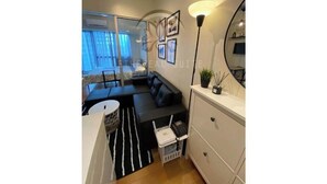 A modern living room with a sofa, a dining table, and a kitchen area with a white cabinet and a mirror. - Acqua Private Residences - Ethereal Suite Room 1 (Makati City)