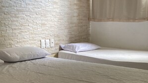 A room with two beds, each with a white mattress and pillow. There is a brick wall and a window with curtains. - Pousada Toco do Mar (Fortaleza)